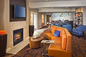 Un hall d’hôtel moderne doté d’une cheminée, de sièges confortables, d’un téléviseur à écran plat et d’un espace bar.