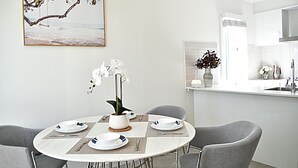 A dining area with a round table set for four, surrounded by grey chairs. A white vase with white flowers is placed on the table. - Elegant & Convenient New House at Leppington - 2 min drive from train station! (Leppington)