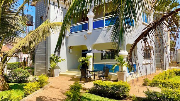 A two-story building with a balcony, a pool area, and a garden with palm trees.