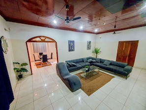 A living room with a sectional sofa, a glass coffee table, and a dining area with chairs and a table. - The Retreat Emerald Apartments close to the beach (Brusubi)