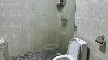 Une salle de bain avec douche, toilettes et carrelage au sol.