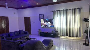 A living room with a sofa, TV, ceiling fan, and curtains.