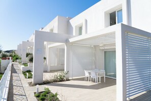 Un edificio moderno blanco con un área de estar al aire libre cubierta y un camino pavimentado.