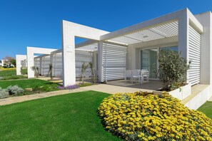 A modern building with a covered outdoor seating area and a garden with yellow flowers. - Stunning Capo Falcone Apartments 2 Bedrooms sleeps 6 (Stintino)