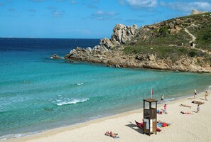 Uma praia com águas turquesa cristalinas, falésias rochosas e uma torre de salva-vidas.