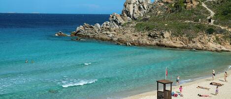 A beach with clear turquoise water, rocky cliffs, and a lifeguard tower.