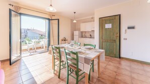 Ein Essbereich mit Tisch für vier Personen, eine Küche im Hintergrund und eine Glastür, die auf einen Balkon mit Gartenmöbeln führt.