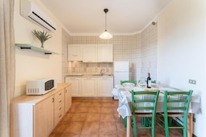A compact kitchen with white cabinets, a microwave, a sink, and a dining area with a table and chairs. - Quaint Residence I Mirti Bianchi 1 Bedroom sleeps 4 no0495 (Santa Teresa Gallura)
