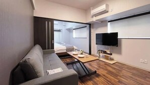 Un espacio habitable moderno y funcional con sofá, televisor de pantalla plana, una mesita y una puerta corredera que da a un dormitorio.