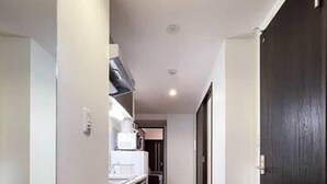 Un pasillo estrecho con suelo de madera, paredes blancas y una puerta negra a la derecha.