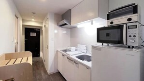 Une cuisine compacte avec des meubles blancs, un four à micro-ondes, un lave-vaisselle et un banc en bois.
