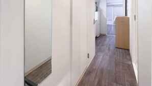 Un couloir étroit avec un plancher en bois, des murs blancs et un grand miroir sur le côté gauche.