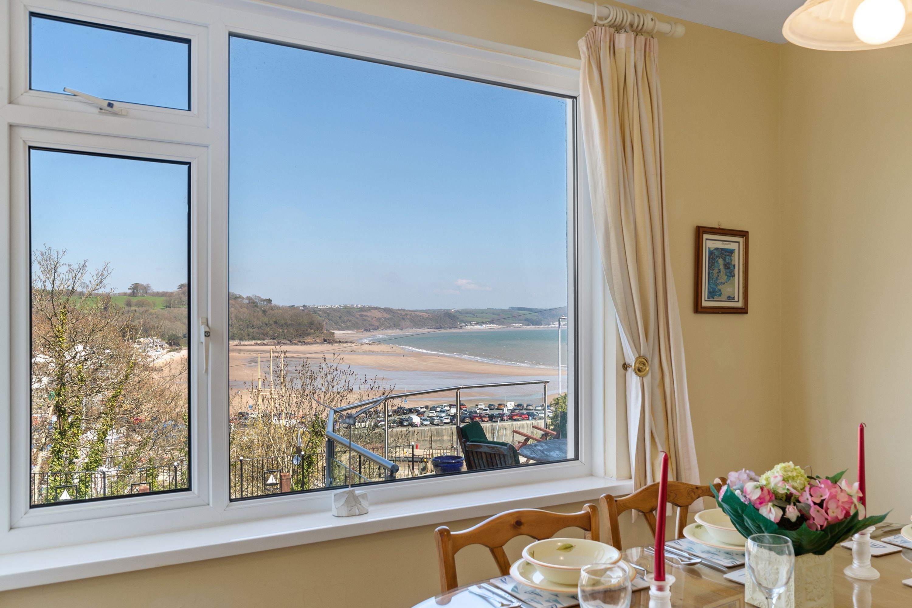 A dining area with a table set for two, a window with a view of the beach, and a framed picture on the wall.