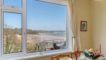 A dining area with a table set for two, a window with a view of the beach, and a framed picture on the wall.