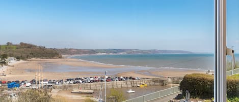 A coastal view from a window overlooking a beach with parked cars and a boat dock.