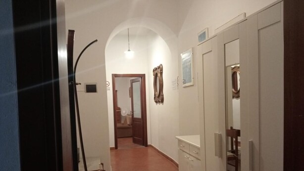 Un couloir étroit au sol carrelé, une porte en bois sur la droite et un meuble blanc avec des tiroirs.