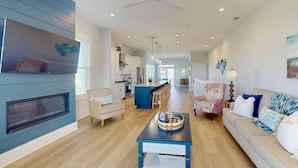A spacious living area with a fireplace, a dining table, and a sofa. - Blue Oasis - New + Modern w/Ocean Views, Pool + Hot Tub, 2 Min Walk to Beach, Elevator, Dogs OK (Carolina Beach)
