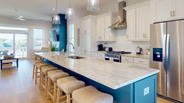 A modern kitchen with a large island, stainless steel appliances, and bar stools. - Blue Oasis - New + Modern w/Ocean Views, Pool + Hot Tub, 2 Min Walk to Beach, Elevator, Dogs OK (Carolina Beach)