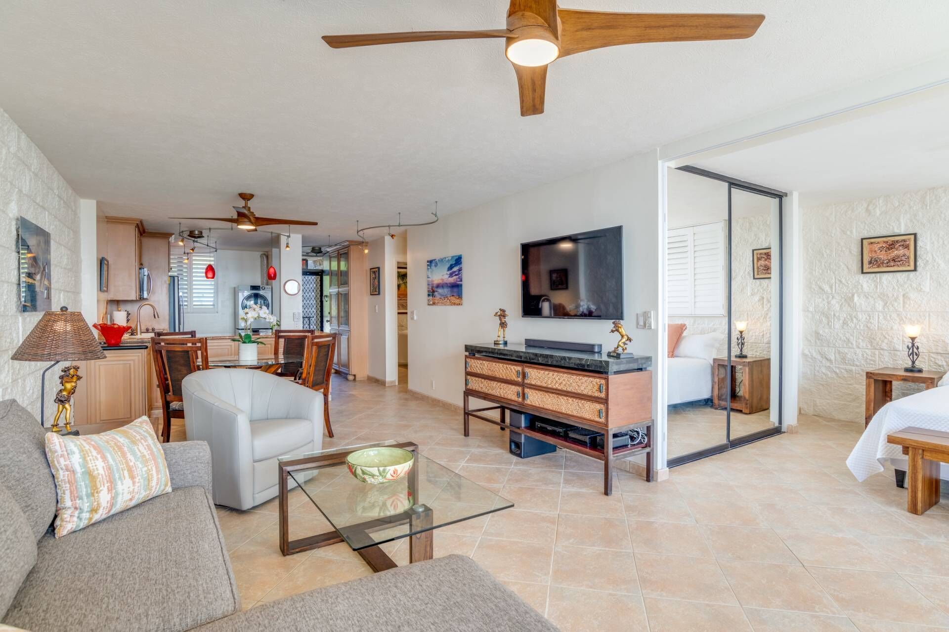A modern living room with a glass coffee table, a sofa, a TV, and a ceiling fan.