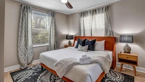 A bedroom with a bed, curtains, a ceiling fan, bedside lamps, and a rug. - Chic Riverfront apartment in downtown San Marco (Jacksonville)