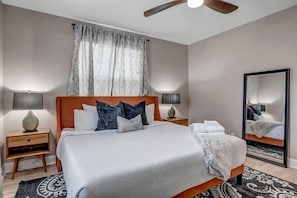 A neatly arranged bedroom with a bed, two bedside tables, a ceiling fan, and a large mirror.
