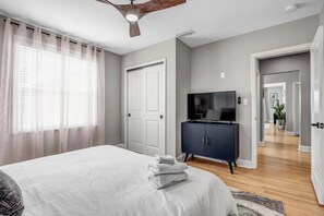 A bedroom with a bed, a TV, a dark cabinet, and a ceiling fan.