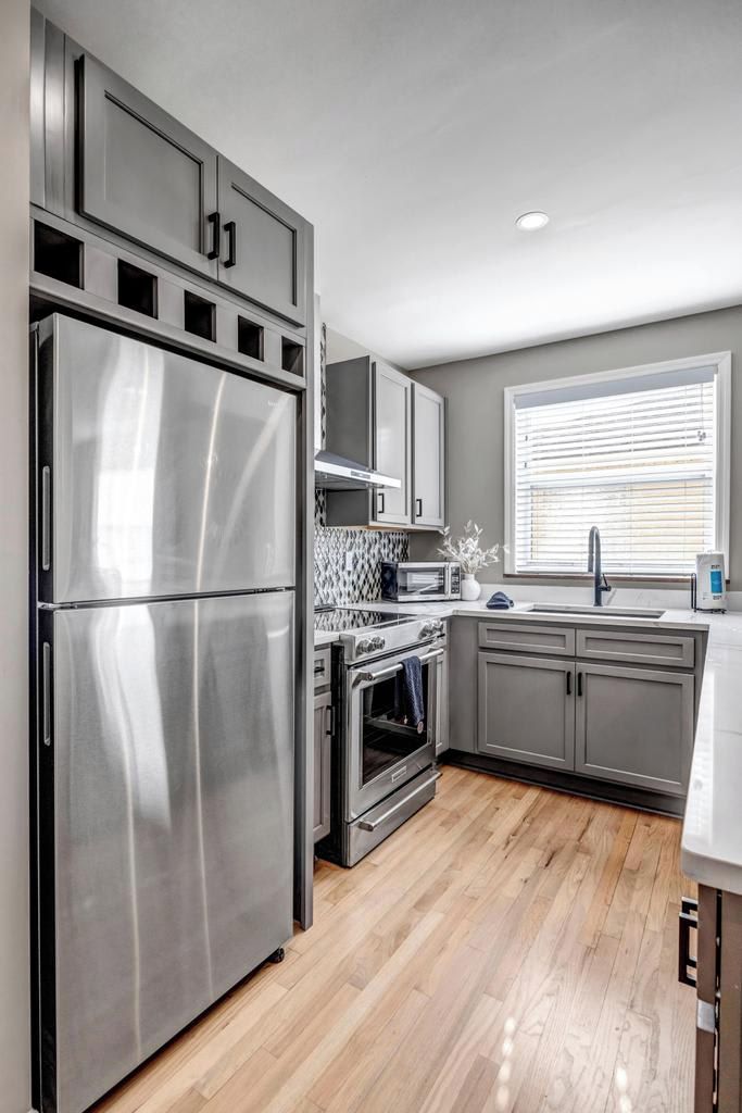 A modern kitchen with stainless steel appliances, grey cabinets, and a wooden floor.