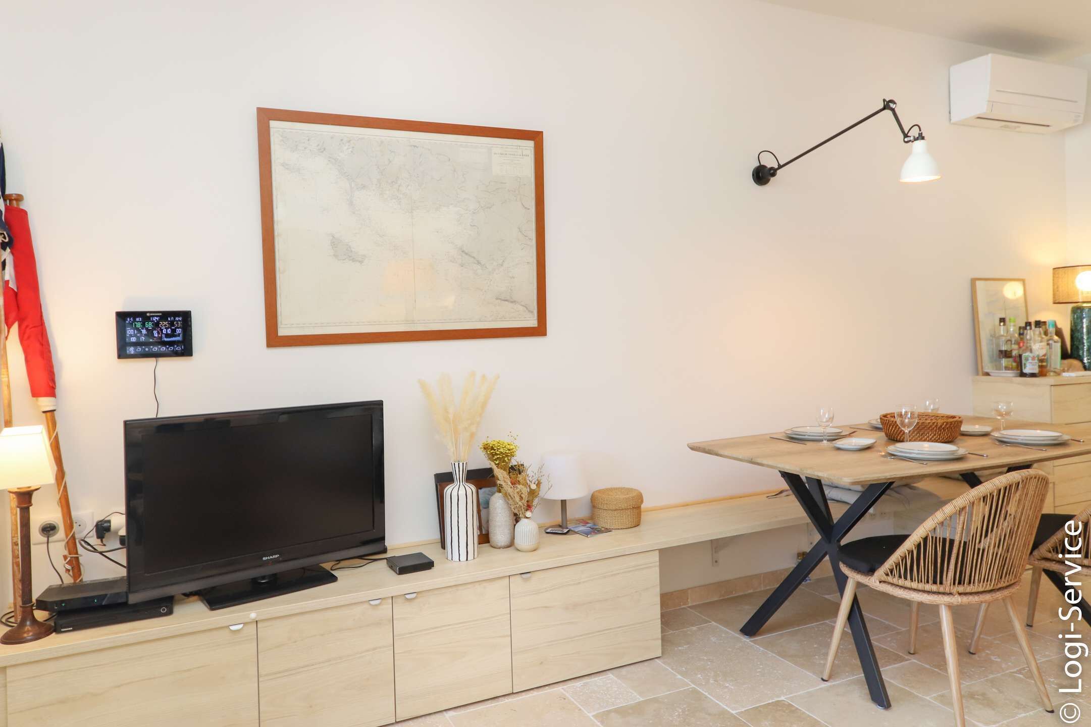 A modern living room with a flat-screen TV, a dining table set with plates and glasses, a map on the wall, and a lamp.