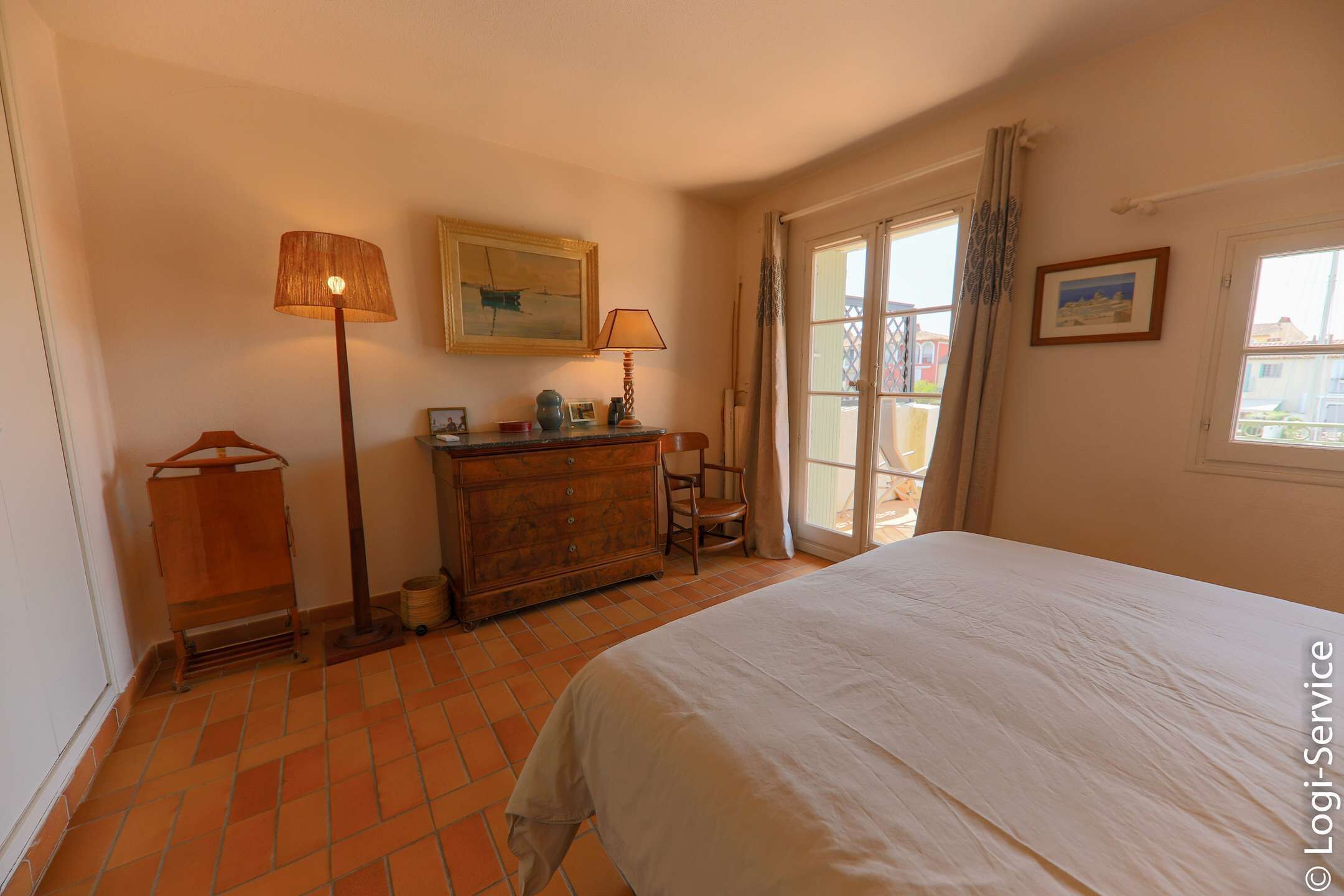Een slaapkamer met een bed, een kaptafel, een lamp en een raam met gordijnen.