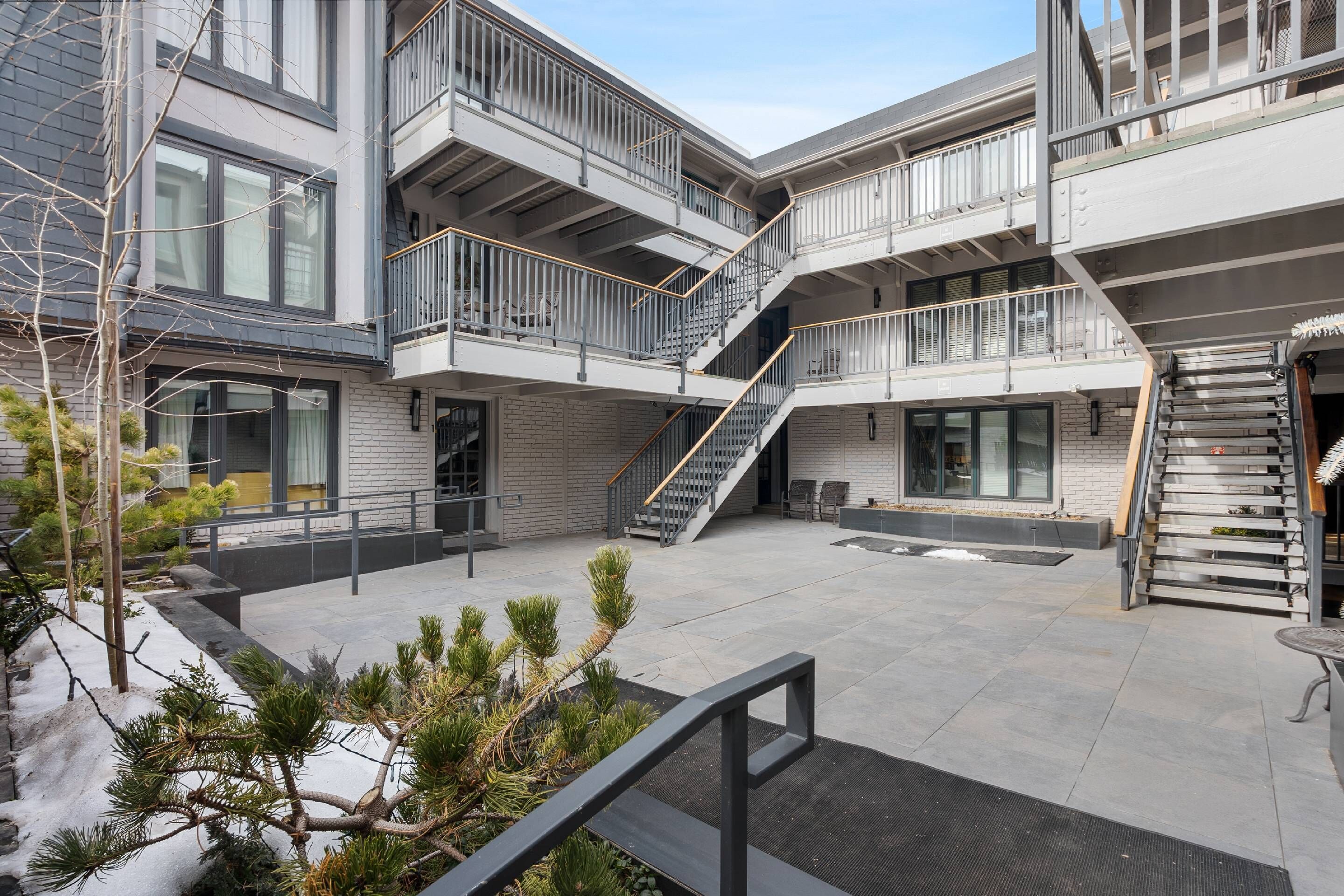 Un bâtiment moderne doté de nombreux balcons, d’escaliers et d’une cour intérieure agrémentée de plantes en pot.