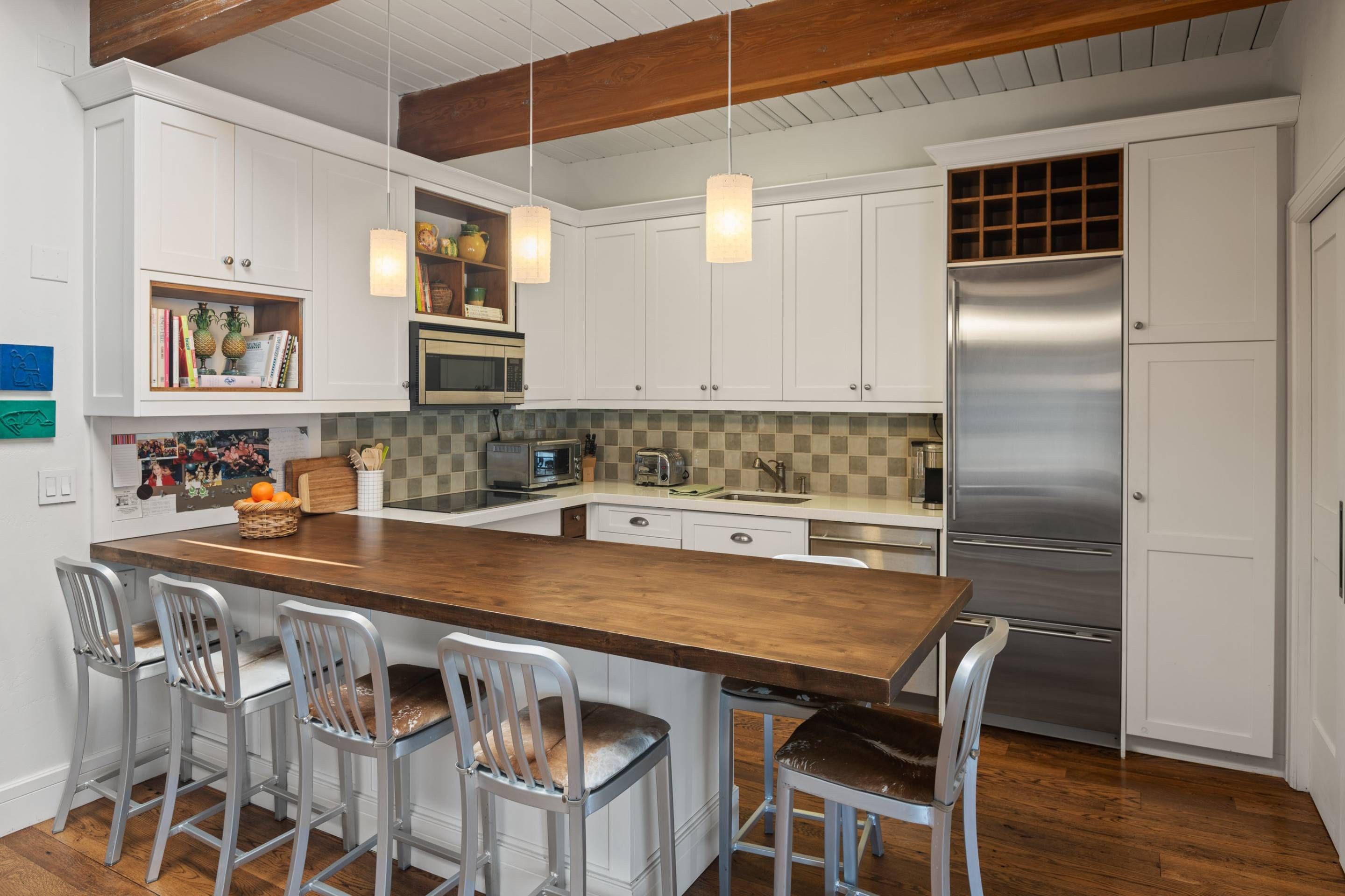 Une cuisine moderne avec des meubles blancs, un îlot central en bois, des appareils électroménagers en acier inoxydable et des luminaires suspendus.