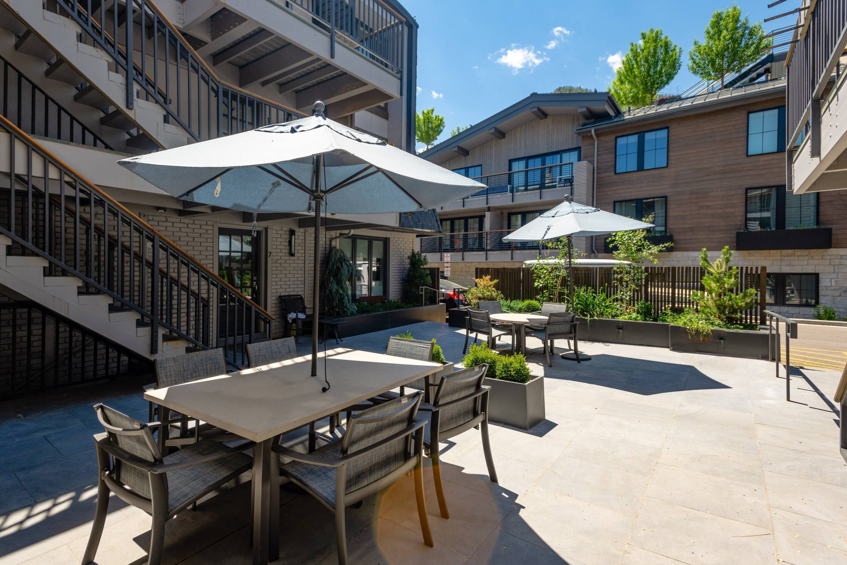 Un espace extérieur aménagé en terrasse, avec une table et des chaises, entouré de plantes en pot et de parasols.
