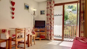 Una habitación acogedora con un escritorio de madera, televisión y balcón con vistas a zonas verdes.