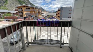 A balcony with a view of a mountainous landscape, a parking area, and buildings with signage for a ski resort.