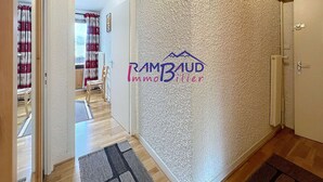 A hallway with a textured wall, a door, and a view into another room with a chair and curtains.