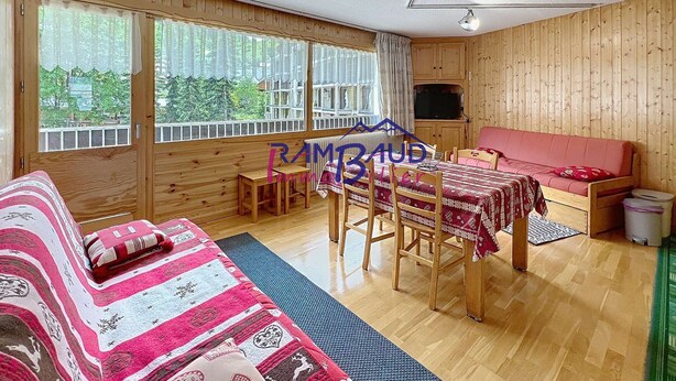 A cozy room with a wooden interior, a sofa, a dining table with chairs, and a television.