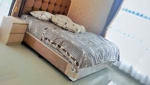 A modern bedroom with a tufted headboard, a large bed with patterned bedding, a bedside table, and a view of the sky through the window. - Homestay Gloria Jogja (Sewon)