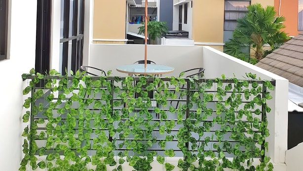 A balcony with a red umbrella, a glass table, and green leafy plants. - Homestay Gloria Jogja (Sewon)