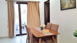 A dining area with a wooden table, beige curtains, and a painting on the wall. - Homestay Gloria Jogja (Sewon)