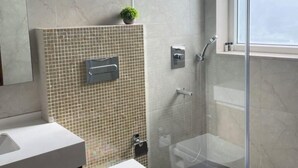 Un baño moderno con cabina de ducha de vidrio, inodoro y lavamanos con salpicadero de azulejos.