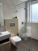 A modern bathroom with a glass shower enclosure, a toilet, and a sink with a tiled backsplash.