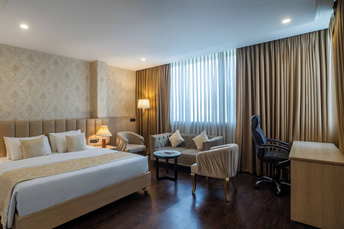 A hotel room with a large bed, two bedside tables, a desk, a chair, and a sofa.