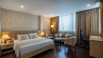 A hotel room with a large bed, two bedside tables, a desk, a chair, and a sofa.