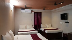 A hotel room with two beds, a ceiling fan, an air conditioning unit, a television, and a desk with a chair. - Sagar Grand (Puducherry)