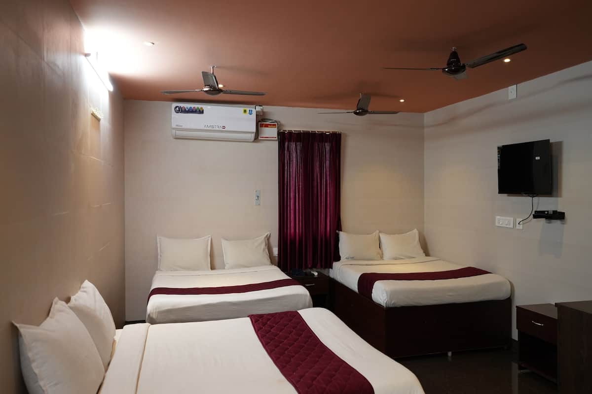 Quarto de hotel com duas camas, ventilador de teto, ar condicionado, televisão e escrivaninha com cadeira.