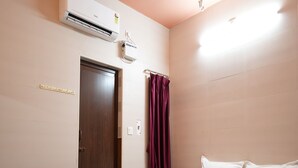 A hotel room with a bed, a wooden door, an air conditioning unit, and a curtain. - Sagar Grand (Puducherry)