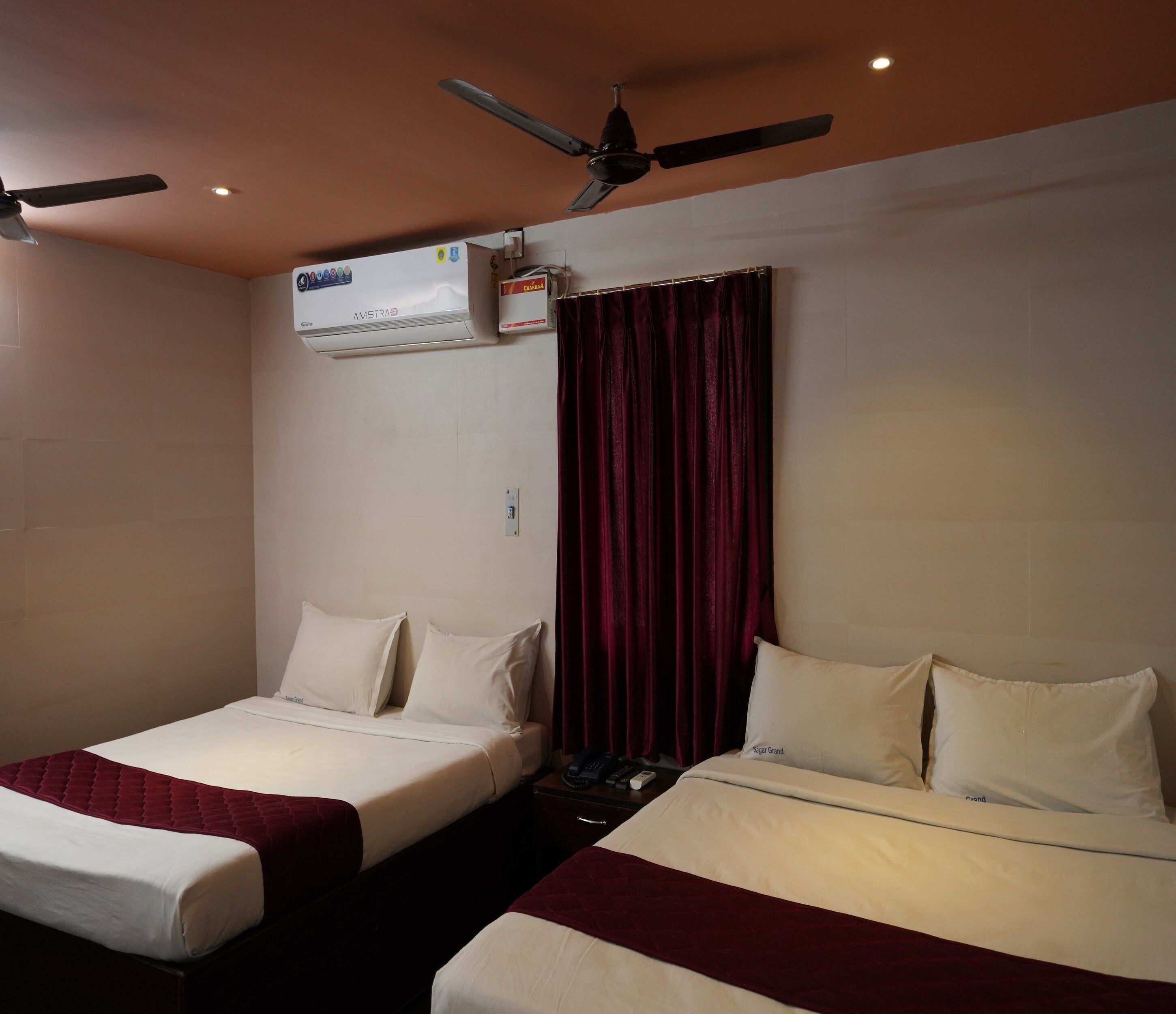 Une chambre d’hôtel avec deux lits simples, un ventilateur de plafond, un climatiseur et un rideau rouge.