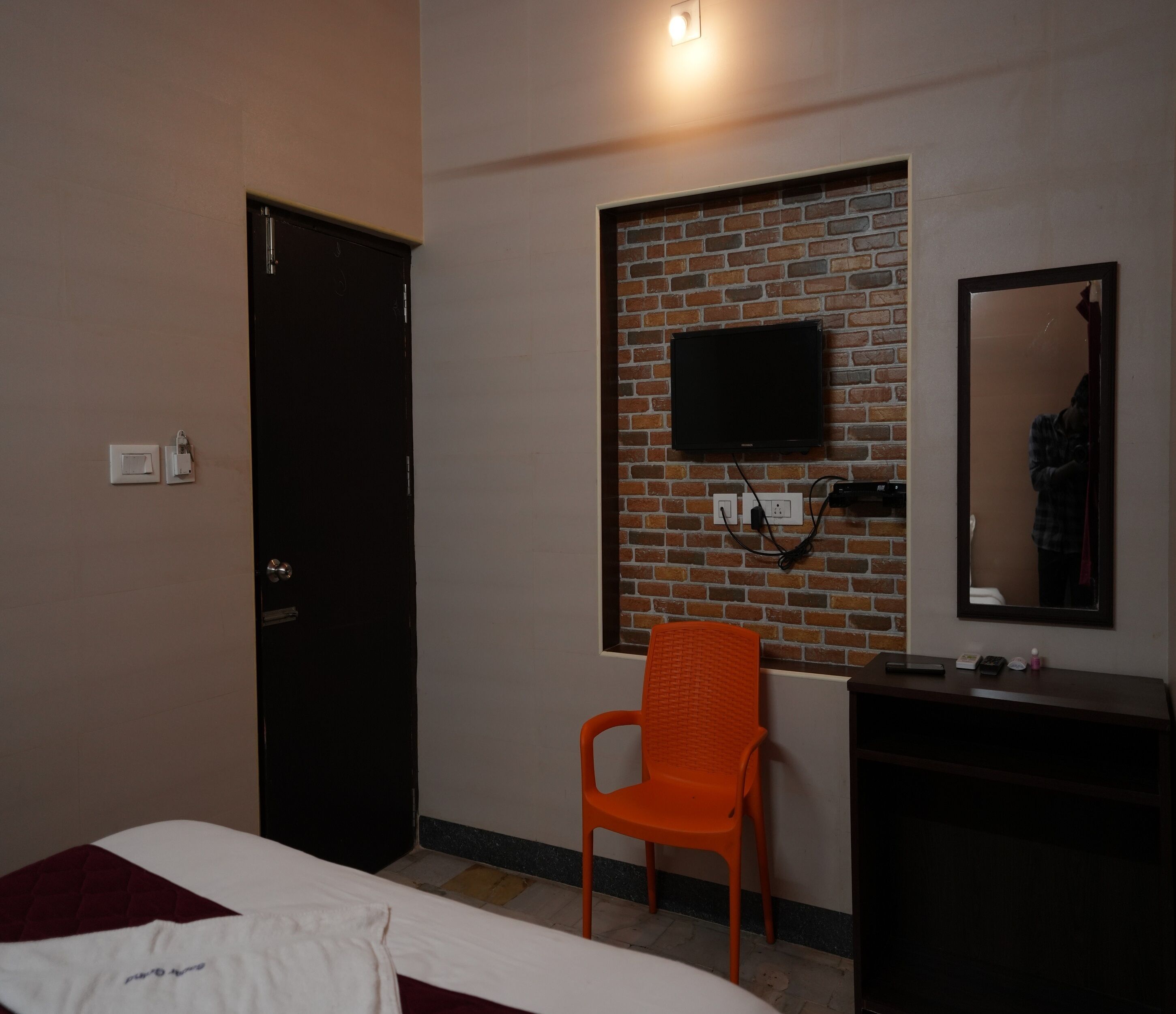 A room with a bed, a chair, a TV mounted on a brick wall, a mirror, and a dresser.