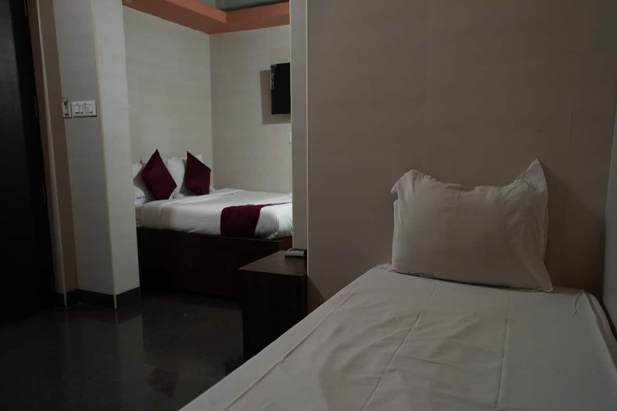 Quarto de hotel com cama, mesa de cabeceira e televisão presa na parede.