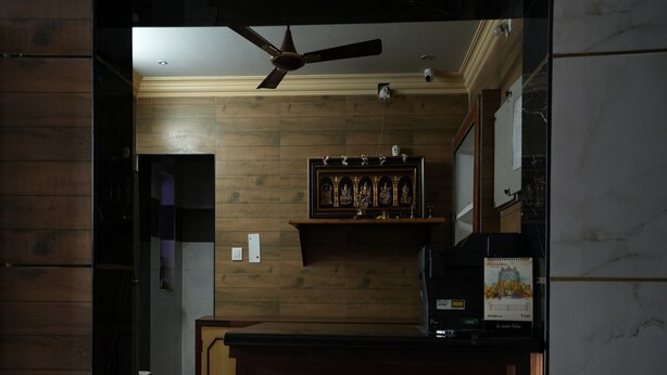 A bar area with a tufted leather bar stool, a ceiling fan, and a wooden wall with a decorative panel. - Sagar Grand (Puducherry)